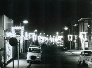 feestverlichting en geparkeerde auto-s in de schoolstraat- rechts de hoek van de erasmusstraat, 5 december 1967kopie